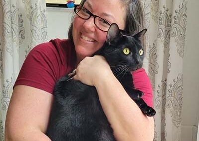 Cat sitter is holding a black cat in her arms.