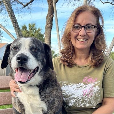 Dog walker is sitting in the park with a large dog. 