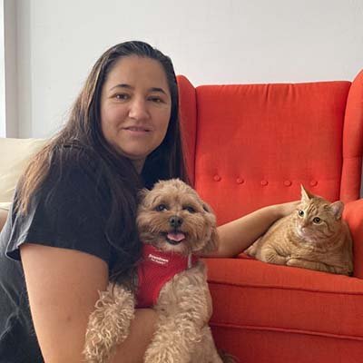 Pet sitter is holding a cat and a dog next to a sofa. 