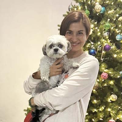 Pet sitter is holding a dog front of a Christmas tree. 